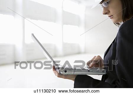 Stock Image - Business woman working on laptop in empty warehouse. Fotosearch