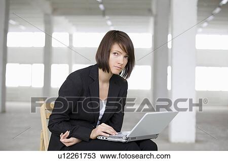 Stock Image - Business woman works on laptop in empty warehouse. Fotosearch