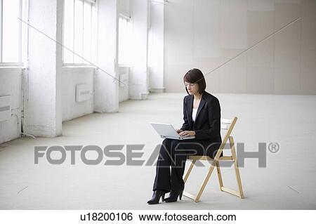 Stock Photograph - Business woman works on laptop in empty warehouse. Fotosearch