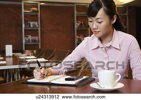 Stock Image - Business woman writing in diary, sitting in cafe. Fotosearch