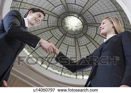 Stock Photo - Businessman and businesswoman shaking hands under dome, low angle view. Fotosearch