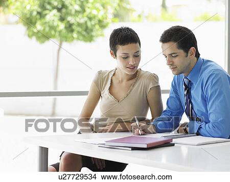 Picture - Businessman and woman at office table going over document information. Fotosearch