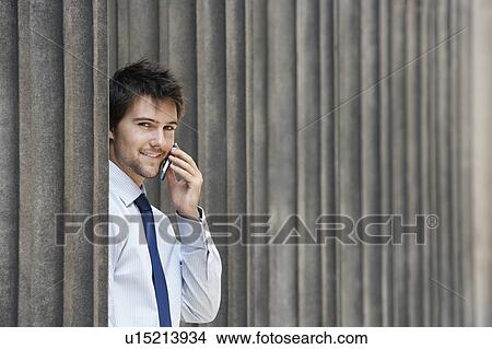 Businessman between pillars outside building talking on phone, portrait View Large Photo Image Picture - Businessman between pillars outside building talking on phone, portrait. Fotosearch