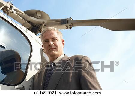 Stock Image - Businessman by helicopter, low angle view. Fotosearch