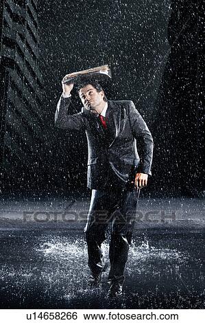 Stock Photograph - Businessman covering head with binder, running through rain. Fotosearch