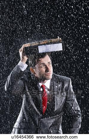 Stock Photograph - Businessman covering head with binder, running through rain. Fotosearch