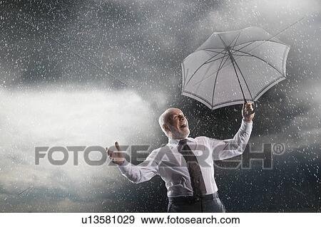 Stock Photo - Businessman holding umbrella, Laughing in Storm, low angle view. Fotosearch