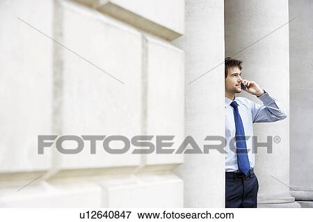 Businessman on cell phone outside building by pillar View Large Photo Image Stock Photo - Businessman on cell phone outside building by pillar. Fotosearch