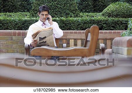 Businessman on park bench reading newspaper and talking on cell phone View Large Photo Image Stock Photography - Businessman on park bench reading newspaper and talking on cell phone. Fotosearch