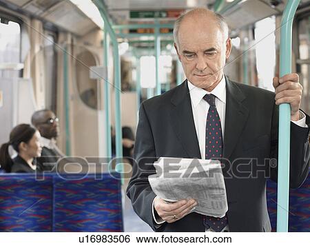 Stock Photograph - Businessman Reading Newspaper on Train, holding onto bar. Fotosearch