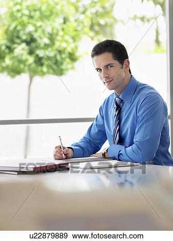 Stock Photo - Businessman sitting at office table writing, portrait. Fotosearch