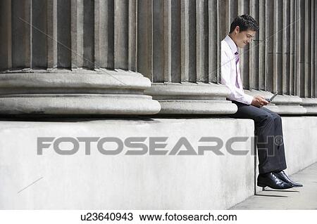 Businessman sitting between pillars outside building sending text message View Large Photo Image Stock Image - Businessman sitting between pillars outside building sending text message. Fotosearch