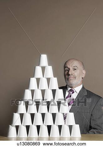 Businessman sitting by pyramid of plastic cups View Large Photo Image Stock Photo - Businessman sitting by pyramid of plastic cups. Fotosearch