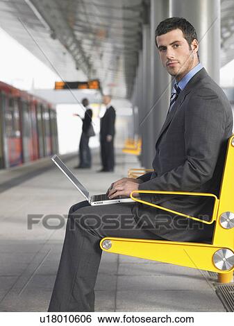 Businessman sitting on bench, working on laptop at Train Station, side view View Large Photo Image Stock Photograph - Businessman sitting on bench, working on laptop at Train Station, side view. Fotosearch