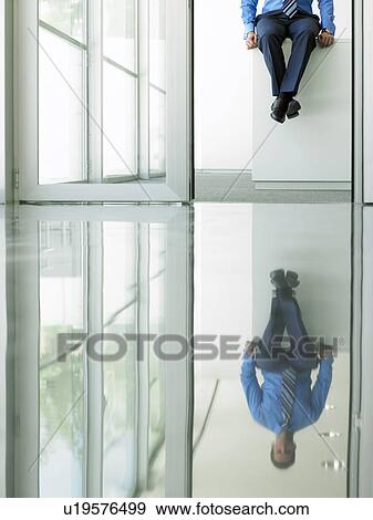 Stock Photo - Businessman sitting on desk in office, low section, viewed through doorway. Fotosearch