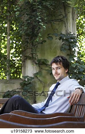 Stock Image - Businessman sitting on park bench relaxing, portrait. Fotosearch