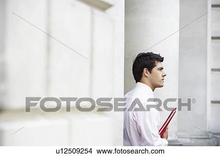 Picture - Businessman sitting on pillar outside building holding files. Fotosearch