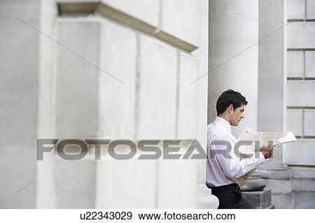 Businessman sitting on pillar reading newspaper outside building View Large Photo Image Stock Photo - Businessman sitting on pillar reading newspaper outside building. Fotosearch