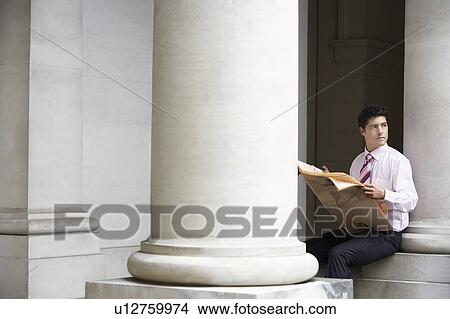 Picture - Businessman sitting on pillar under entablature reading newspaper. Fotosearch