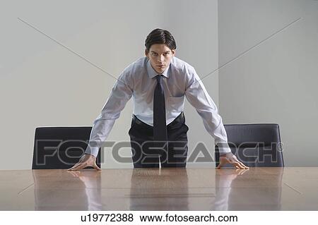 Businessman standing and leaning over conference room table View Large Photo Image Stock Photo - Businessman standing and leaning over conference room table. Fotosearch