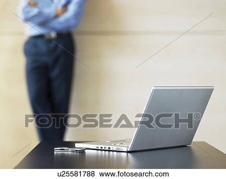 Stock Photo - Businessman standing by laptop and Cell Phone on desk, focus on foreground. Fotosearch