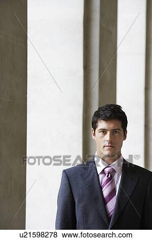 Stock Photo - Businessman standing by pillars outside building, portrait. Fotosearch