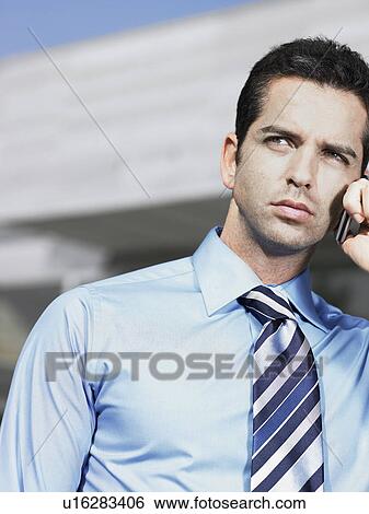 Businessman standing in plaza using cell phone View Large Photo Image Stock Photograph - Businessman standing in plaza using cell phone. Fotosearch