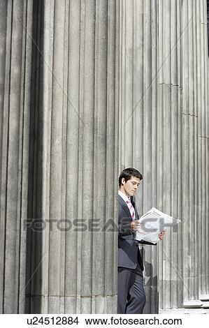 Businessman standing outside building between pillars reading newspaper View Large Photo Image Picture - Businessman standing outside building between pillars reading newspaper. Fotosearch