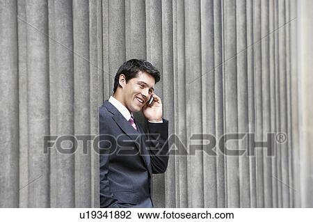 Businessman standing outside building between pillars on cell phone View Large Photo Image Stock Image - Businessman standing outside building between pillars on cell phone. Fotosearch