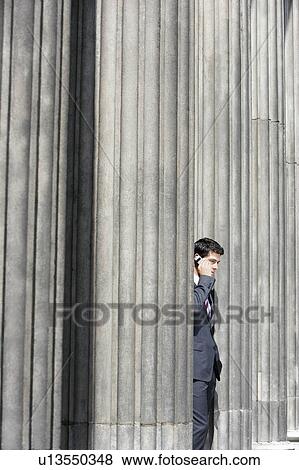 Businessman standing outside building between pillars on cell phone View Large Photo Image Stock Photo - Businessman standing outside building between pillars on cell phone. Fotosearch