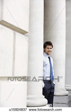 Stock Photo - Businessman standing outside building by pillar, portrait. Fotosearch