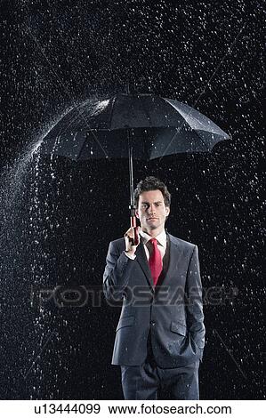 Stock Photo - Businessman standing under sturdy Umbrella, hand in pocket. Fotosearch