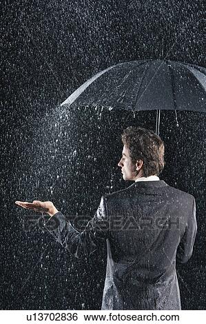 Businessman sticking hand out from under umbrella to feel rain, back view View Large Photo Image Stock Photograph - Businessman sticking hand out from under umbrella to feel rain, back view. Fotosearch