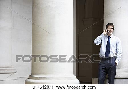Businessman talking on cell phone by building pillar View Large Photo Image Stock Image - Businessman talking on cell phone by building pillar. Fotosearch