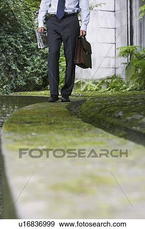Stock Photo - Businessman walking on wall in park, low section. Fotosearch