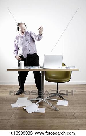 Businessman with earphones fooling around at desk View Large Photo Image Stock Image - Businessman with earphones fooling around at desk. Fotosearch
