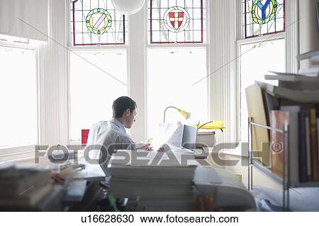 Stock Image - Businessman works from desk in bay window. Fotosearch