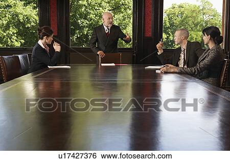 Stock Photograph - Businesspeople meeting around boardroom table, businessman standing. Fotosearch