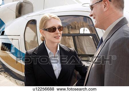 Stock Photo - Businesspeople standing beside helicopter. Fotosearch