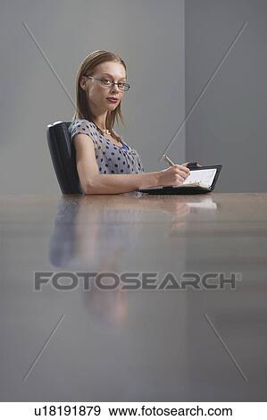 Businesswoman sitting at table writing in appointment calendar View Large Photo Image Stock Photo - Businesswoman sitting at table writing in appointment calendar. Fotosearch