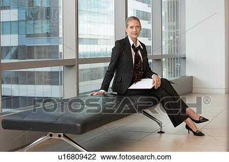 Stock Image - Businesswoman sitting in office lobby, portrait. Fotosearch