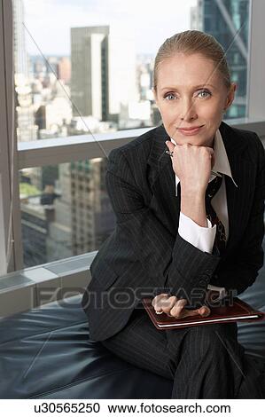 Stock Image - Businesswoman sitting in office lobby, portrait. Fotosearch