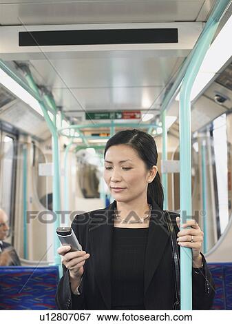Stock Photo - Businesswoman Using Cell Phone, holding onto bar on Train. Fotosearch