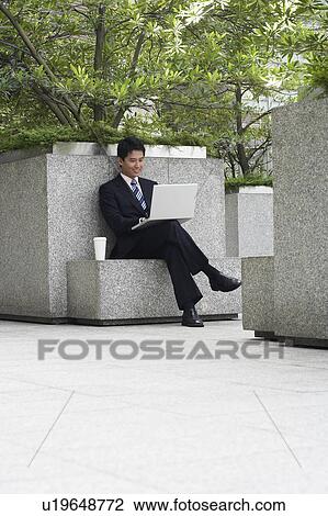 Stock Image - China, Hong Kong, business man sitting on stone bench using laptop. Fotosearch