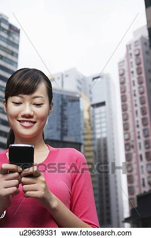 Stock Image - China, Hong Kong, woman text messaging on street. Fotosearch