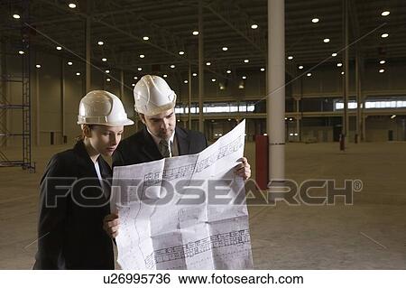 Stock Photograph - Colleagues study blueprint in empty warehouse. Fotosearch