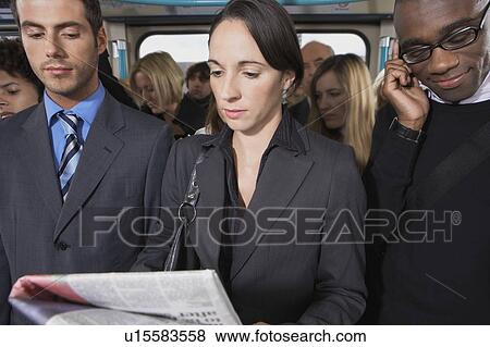 Stock Photo - Commuters standing on train, reading newspapers, talking on mobiles. Fotosearch