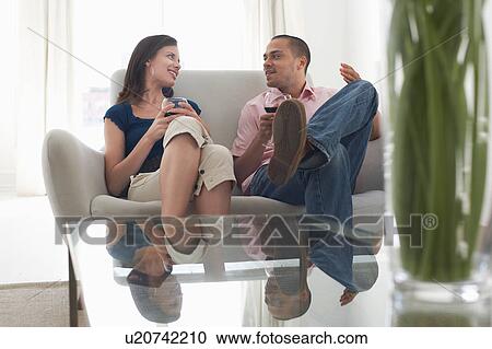 Stock Image - Couple drinking wine, talking on sofa. Fotosearch