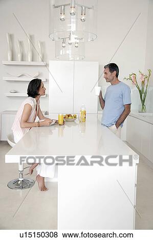 Stock Photo - Couple eating breakfast at kitchen bench, side view. Fotosearch
