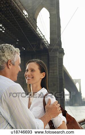 Stock Image - Couple embracing under Brooklyn Bridge. Fotosearch